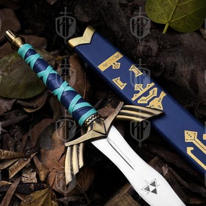 Pode incluir: Espada de fantasia com l&acirc;mina branca e detalhes dourados. O punho &eacute; envolto em couro azul e turquesa. A bainha azul apresenta padr&otilde;es dourados. A espada est&aacute; sobre um leito de folhas e galhos.