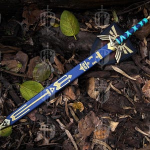 Pode incluir: Uma espada de fantasia azul e dourada com um escudo. A espada tem uma l&acirc;mina azul com detalhes dourados e uma guarda dourada. O escudo &eacute; preto com detalhes dourados e brancos. A espada e o escudo est&atilde;o sobre folhas e madeira.