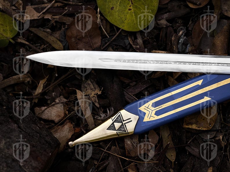 Pode incluir: Uma l&acirc;mina de espada prateada repousa sobre uma bainha azul com detalhes dourados. A bainha apresenta um design geom&eacute;trico dourado e uma ponta dourada. A espada e a bainha s&atilde;o colocadas sobre um fundo de folhas e galhos.