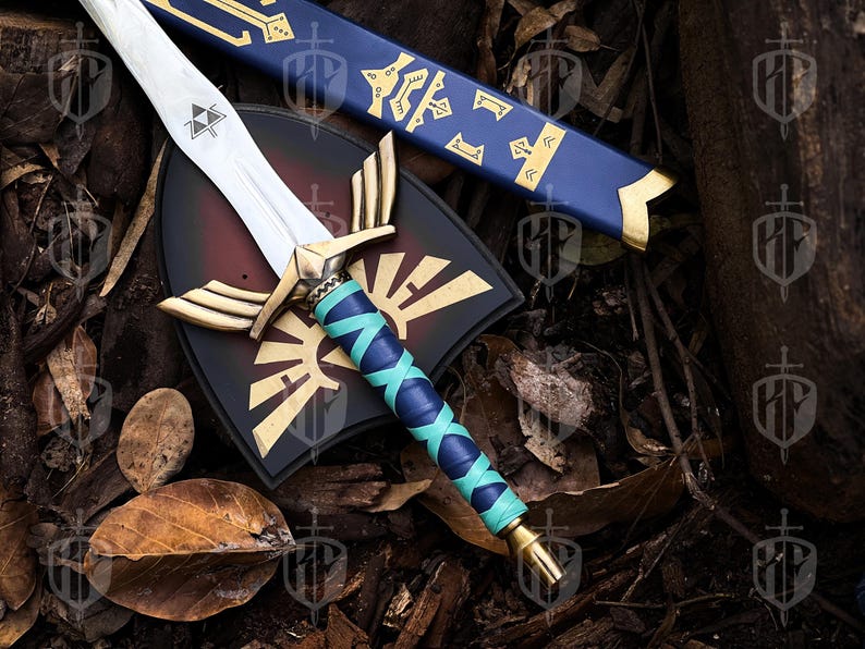 Pode incluir: R&eacute;plica detalhada de uma espada, escudo e bainha de fantasia. A espada apresenta uma l&acirc;mina prateada, detalhes dourados e uma empunhadura enrolada em azul e verde-azulado. O escudo &eacute; preto e vermelho com um emblema dourado.