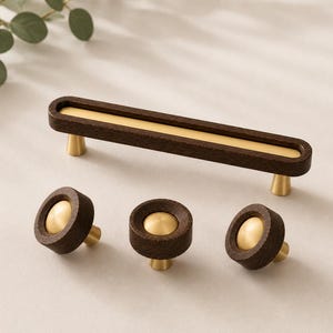 May include: A set of modern cabinet hardware featuring a long, rectangular pull and three round knobs. The hardware is made of dark wood with brass accents, creating a contrasting color scheme. The knobs and pull are designed for easy installation and use.