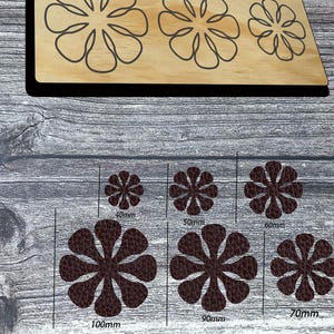 May include: Wooden flower-shaped die cuts in various sizes. The die cuts are arranged on a wooden board, with outlines of flowers on the top and cut-out flowers below. Sizes are labeled in millimeters, ranging from 40mm to 100mm.