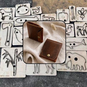 May include: Two brown leather wallets with snap closures are displayed over a collection of various metal cutting dies mounted on wooden blocks, featuring shapes like animals, tools, and plants with visible identification codes.