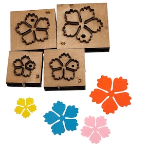 May include: Wooden flower-shaped die cut blocks with metal outlines, numbered 35, 45, 55, and 65. Also, cut-out flowers in yellow, blue, orange, and pink are displayed. These are likely for crafting or scrapbooking.
