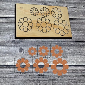 May include: A rectangular wooden die cutting board labeled 722 featuring six flower-shaped outlines. Below the board are six corresponding orange felt flower cutouts with labeled sizes ranging from 50mm to 100mm in diameter.