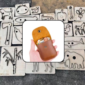 May include: A small, tan leather pouch with a snap button closure, containing several coins and cards. The pouch is surrounded by various metal cutting dies mounted on wooden blocks, each featuring unique shapes like animals and plants.