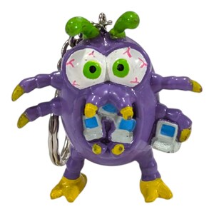 May include: A purple monster keychain featuring large white eyes with red veins, bright green pupils, and two green antennae. The creature has multiple arms, yellow feet, and is holding a small gray and blue computer in one of its hands.
