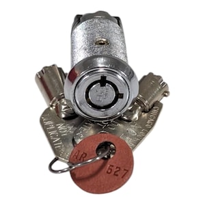 Puede incluir: Un mecanismo de cerradura cilíndrico de color plateado con una entrada de llave circular, acompañado de tres llaves de metal. Las llaves tienen el texto "CHICAGO LOCK CO" y "DO NOT DUPLICATE". Una etiqueta redonda de color marrón rojizo con "AR 527" está unida.