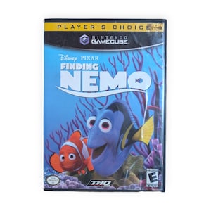 Può includere: Una custodia per videogioco Nintendo GameCube di Disney Pixar Finding Nemo. La copertina mostra Dory e Nemo su uno sfondo di barriera corallina blu. Il banner superiore riporta Player's Choice e l'angolo inferiore mostra la classificazione ESRB Everyone.