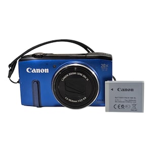 Puede incluir: Una cámara digital Canon azul con lente de zoom óptico 20x y correa de muñeca negra, acompañada de una batería Canon NB-6L gris. El lente está marcado con 4.5-90.0mm 1:3.5-6.8, y el cuerpo de la cámara muestra el logo y el modelo.