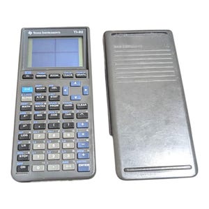 Op de afbeelding: Een donkergrijze Texas Instruments TI-82 grafische rekenmachine met een blauwachtig scherm en een bijpassende donkergrijze beschermkap. Het apparaat is voorzien van een numeriek toetsenbord en functietoetsen met blauwe labels.