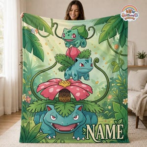 May include: A soft fleece blanket featuring a vertical progression of three green creatures in a jungle setting. The design includes large tropical leaves, small flowers, and the word NAME in the bottom right corner with a logo at the top right.