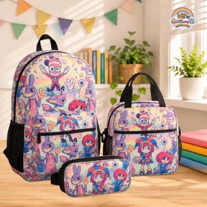 Op de afbeelding: Een set bestaande uit een rugzak, lunchtas en etui met een pastelkleurige regenboogachtergrond en een herhalend patroon van stripfiguren, waaronder een nar en een konijn, allemaal voorzien van zwarte ritsen en afwerking.