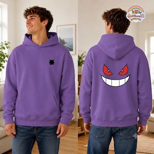 May include: A purple hooded sweatshirt featuring a small black silhouette of a creature on the left chest and a large graphic on the back displaying a wide, grinning face with sharp red eyes and a white mouth filled with pointed teeth.