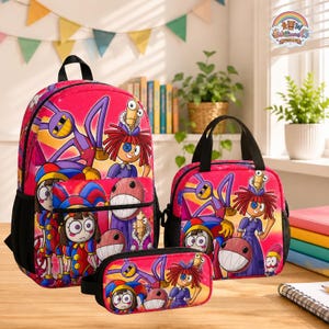 Op de afbeelding: Een set bestaande uit een felroze rugzak, lunchtas en etui met een kleurrijke grafische print van stripfiguren met grote ogen, rood haar en paarse ledematen, elk voorzien van zwarte details en zijvakken van gaas.
