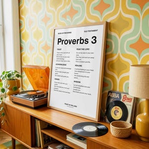 Peut inclure: Un meuble en bois avec une affiche encadrée de Proverbes 3, un tourne-disque et des disques vinyles. L'affiche est dans un cadre en bois et contient du texte. Une lampe avec un abat-jour beige est posée sur le meuble.