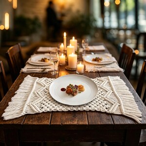 May include: A rustic wooden dining table set for a meal. The table is adorned with white plates, macrame placemats, candles, and glassware. The plates hold food, and the scene is lit by candlelight, creating a warm ambiance.