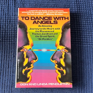May include: A paperback book titled "TO DANCE WITH ANGELS" with a colorful cover. The cover features two pixelated faces facing each other, with a rainbow and blue background. The book's title and author's names are prominently displayed.