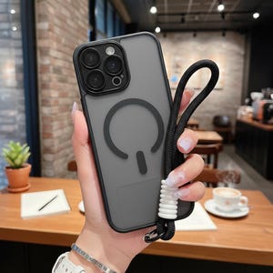 May include: A clear phone case with a black border and a black lanyard. The case has a gray backing with a circular design. The lanyard is black with a white and silver accent. The phone case is held by a person.