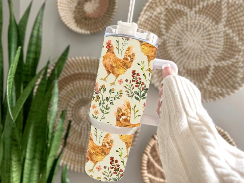 May include: A stainless steel tumbler with a chicken and floral pattern. The tumbler has a white handle and a clear lid with a straw. The design features watercolor illustrations of chickens, flowers, and foliage on a cream background.