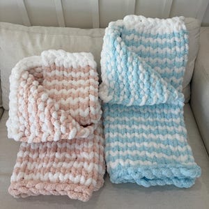 Peut inclure: Deux couvertures faites &agrave; la main, l'une rose et blanche, l'autre bleue et blanche. Les couvertures ont un motif boucl&eacute; textur&eacute;. Elles sont pli&eacute;es et pr&eacute;sent&eacute;es sur un canap&eacute; de couleur neutre.