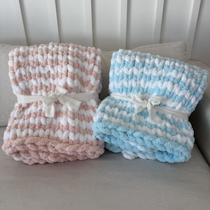 Peut inclure: Deux couvertures en tricot &eacute;pais, une rose et blanche, l'autre bleue et blanche. Chacune est attach&eacute;e avec un ruban blanc. Les couvertures sont pli&eacute;es et semblent &ecirc;tre faites d'une mati&egrave;re moelleuse, id&eacute;ale pour un b&eacute;b&eacute; ou un enfant.