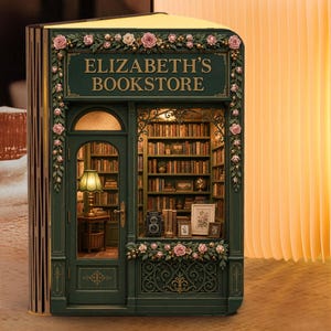 May include: A book-shaped lamp featuring a dark green facade labeled ELIZABETH'S BOOKSTORE with floral accents and a miniature interior view of a library. The lamp emits a warm, soft glow from its accordion-style pages, creating a book-like structure.
