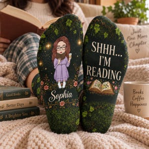 May include: A pair of dark green socks featuring a printed illustration of a person with glasses reading a book while holding a cup, the name Sophia, and the text SHHH... I'M READING, surrounded by ivy vines, small flowers, and glowing lights.
