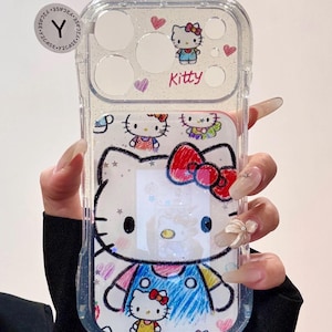 Op de afbeelding: Transparante telefoonhoes met een Hello Kitty-ontwerp. De hoes heeft een transparante, glinsterende achtergrond met een grote Hello Kitty-illustratie in het midden, en kleinere afbeeldingen en het woord "Kitty" bovenaan. De hoes heeft een kattenoordesign aan de bovenkant.