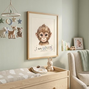 May include: A framed print with a monkey illustration and the text "I am LOVED" and Jeremiah 31:3. A wooden changing table with a changing mat, bibs, and a ceramic bunny figurine. A mobile with felt stars, moons, and animal figures.