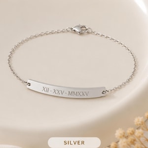 May include: A silver-toned metal chain bracelet featuring a curved horizontal bar plate. The plate is engraved with the Roman numerals XII · XXV · MMXXV. The bracelet includes a small lobster claw clasp for secure fastening and a polished finish.