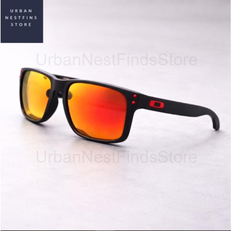 Puede incluir: Gafas de sol negras con lentes espejadas naranja-rojo. Las gafas tienen una montura cuadrada con detalles rojos en las patillas y el logotipo de la marca. Las lentes reflejan un color naranja brillante.