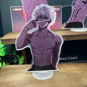 May include: A clear acrylic standee featuring a shirtless anime character with white hair and a blindfold. The character is holding the blindfold up with one hand. The standee is on a clear base. Other standees are in the background.