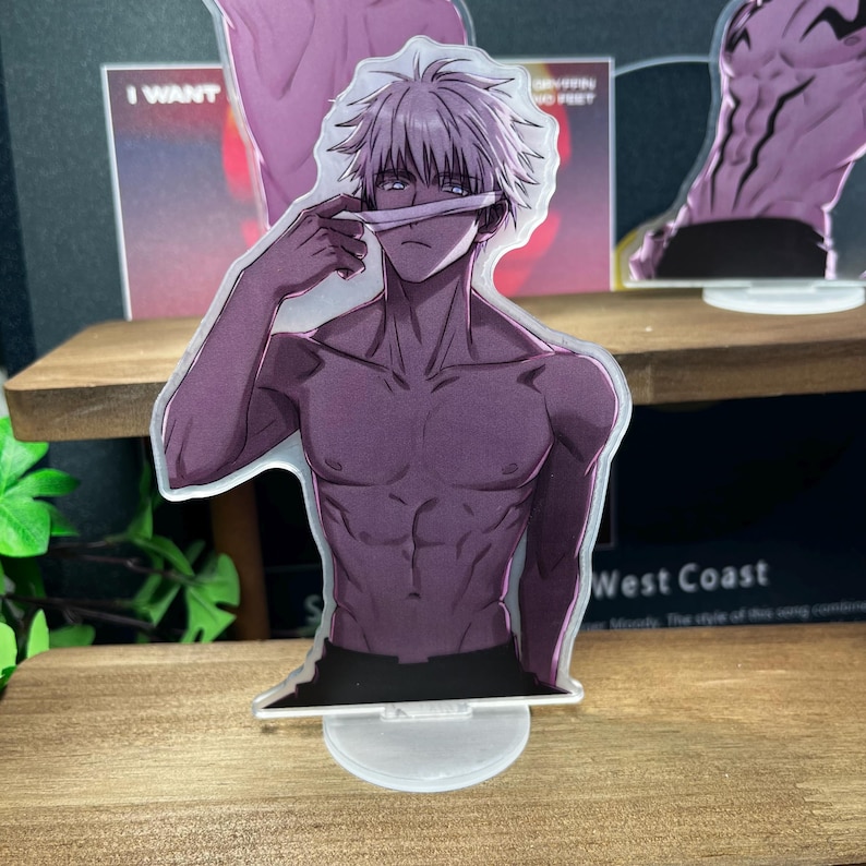 May include: A clear acrylic standee featuring a shirtless anime character with white hair and a blindfold. The character is holding the blindfold up with one hand. The standee is on a clear base. Other standees are in the background.