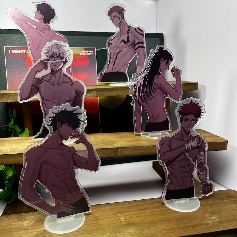 May include: Acrylic standees featuring anime characters in various poses. The figures are semi-transparent with a purple and black color scheme. Some standees have text on the background. The standees are displayed on a wooden shelf.