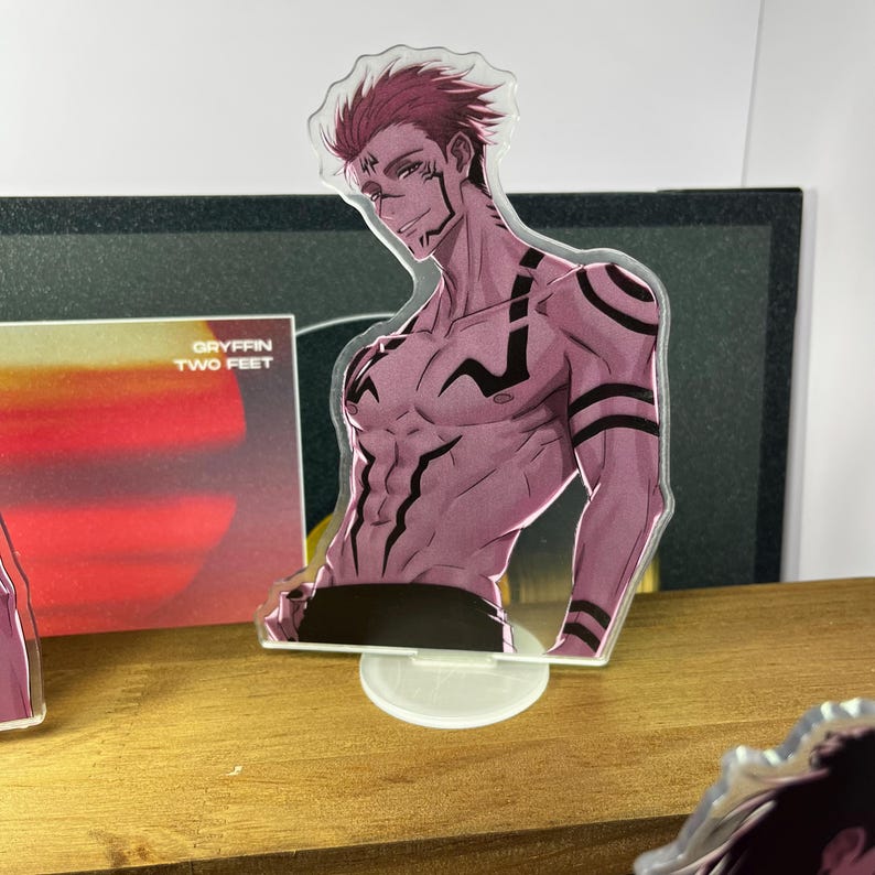 May include: A clear acrylic standee featuring a muscular anime character with red hair and black markings. The standee is on a clear base. The text "GRYFFIN TWO FEET" is visible on a card behind the standee.