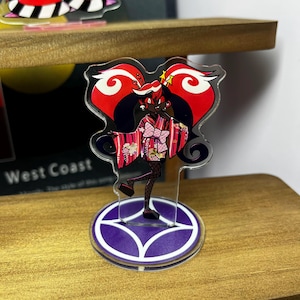May include: A clear acrylic standee featuring a stylized anime character in a pink kimono with a bow. The character has black hair and is set against a red and black background. The standee is on a purple base with white accents.