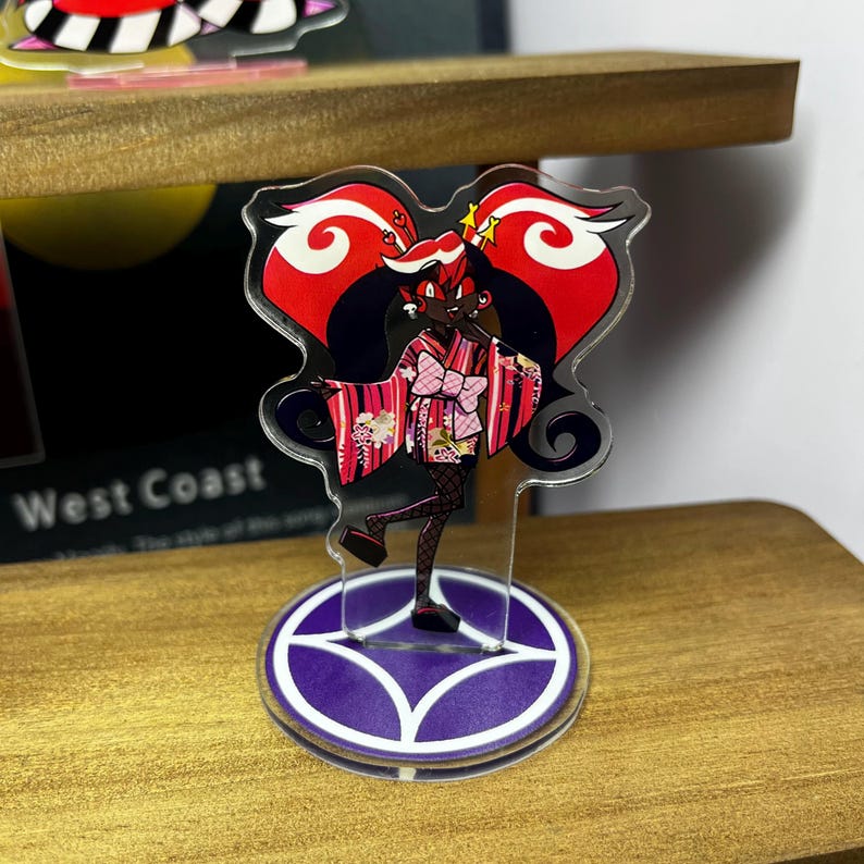 May include: A clear acrylic standee featuring a stylized anime character in a pink kimono with a bow. The character has black hair and is set against a red and black background. The standee is on a purple base with white accents.