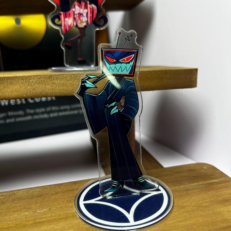 May include: A clear acrylic figure of a character with a TV screen head, wearing a dark blue suit with pinstripes. The figure has a red and blue face with sharp teeth and is holding a teal object. The base is a dark blue circle with a white design.