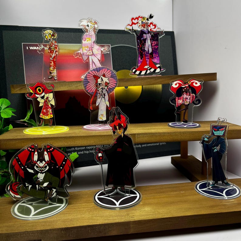 May include: A collection of acrylic character figures, each with a unique design and vibrant colors. The figures are displayed on a wooden shelf, showcasing various anime-style characters in detailed outfits and poses. The figures are on clear circular or oval bases.