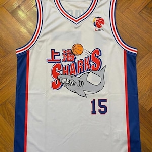 May include: White basketball jersey with blue and red accents. Features the text "上海 SHARKS" and a shark graphic with the number 15. The jersey has a V-neck and the CBA logo.