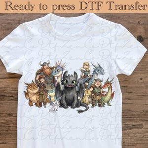 以下が含まれることがあります： 「ヒックとドラゴン」のキャラクターが描かれた、カラフルなグラフィックの白いTシャツ。デザインにはドラゴンとバイキングのキャラクターが含まれています。「Ready to press DTF Transfer」の文字が上部にあります。