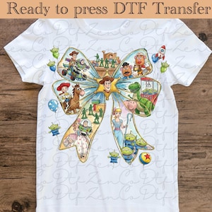 Peut inclure: T-shirt blanc avec un motif coloré en forme de nœud orné de personnages de Toy Story. Le motif comprend Woody, Buzz l'Éclair et d'autres personnages. Le texte en haut indique "Ready to press DTF Transfer".