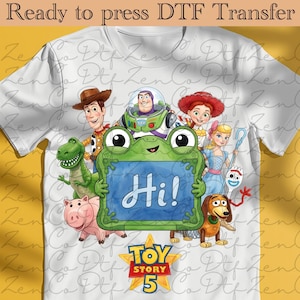 Peut inclure: Un t-shirt blanc avec un graphique coloré des personnages de Toy Story, dont Woody, Buzz l'Éclair, Jessie, Rex, Bayonne, la Bergère, Fourchette et Zigzag. Un cadre vert en forme de grenouille affiche le texte Hi! avec le logo Toy Story 5 en dessous.