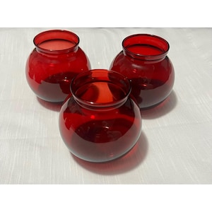 May include: Three matching round glass vases in a deep, translucent red colour. Each vase features a wide, spherical body that tapers towards a circular opening at the top with a smooth, slightly flared rim. The glass is clear and uniform in tone.