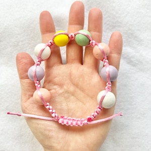 May include: A pink string bracelet with colorful wooden beads. The beads are in shades of pink, purple, green, yellow, and white.