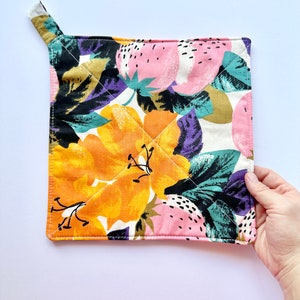 May include: A quilted hot pad with a floral print featuring pink, orange, green, and purple flowers. The hot pad has a loop handle.