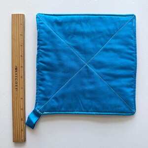 May include: A square, turquoise pot holder with white stitching and a hanging loop. The pot holder measures approximately 7 inches by 7 inches. The stitching forms an X across the center of the pot holder.