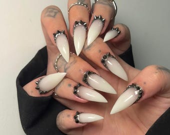 Uñas postizas blancas estilo stiletto, juego gótico con tachuelas cromadas.
