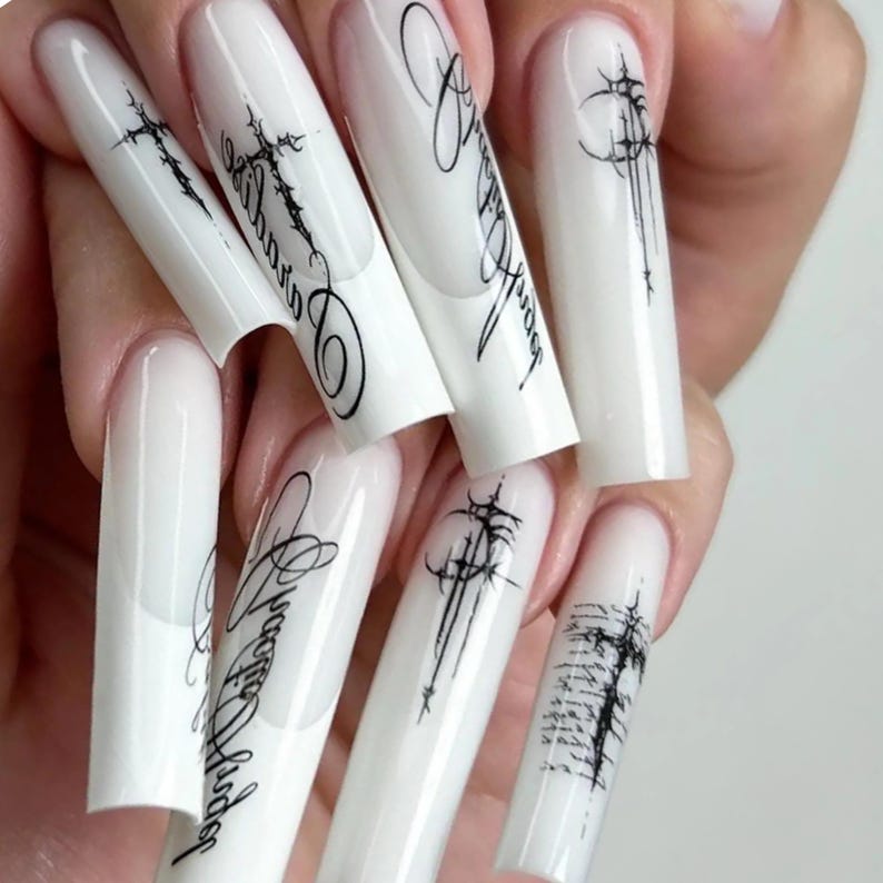 Pode incluir: Unhas artificiais longas e brancas com escrita preta e desenhos abstratos. As unhas s&atilde;o brancas brilhantes com um design de ponta francesa. A escrita preta parece ser uma assinatura ou um nome estilizado. Os desenhos abstratos s&atilde;o lineares e art&iacute;sticos.